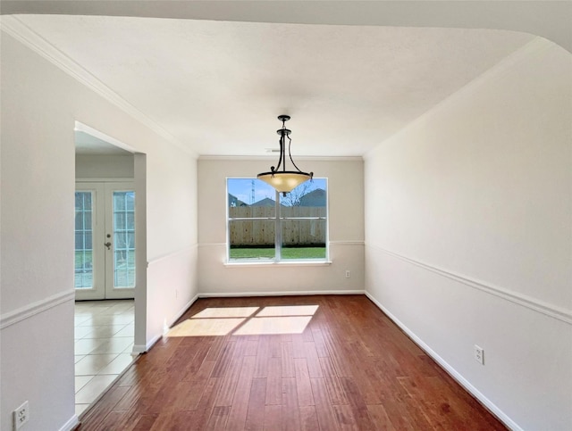 unfurnished dining area with french doors, arched walkways, baseboards, wood finished floors, and ornamental molding