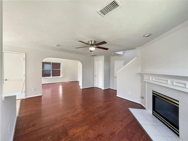 unfurnished living room featuring wood finished floors, visible vents, a fireplace, arched walkways, and ceiling fan