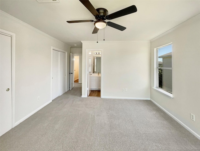 unfurnished bedroom with crown molding, multiple closets, carpet floors, baseboards, and ensuite bath