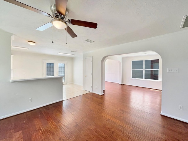 spare room with wood finished floors, ceiling fan, arched walkways, baseboards, and visible vents
