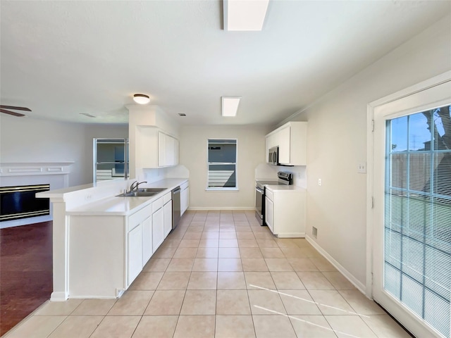 kitchen featuring a sink, light countertops, a fireplace, a peninsula, and appliances with stainless steel finishes