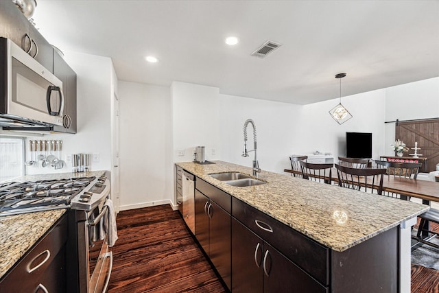 kitchen with a barn door, appliances with stainless steel finishes, a peninsula, dark wood-style floors, and a sink