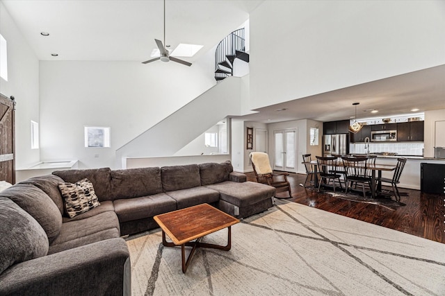 living area featuring ceiling fan, a barn door, a high ceiling, and dark wood finished floors