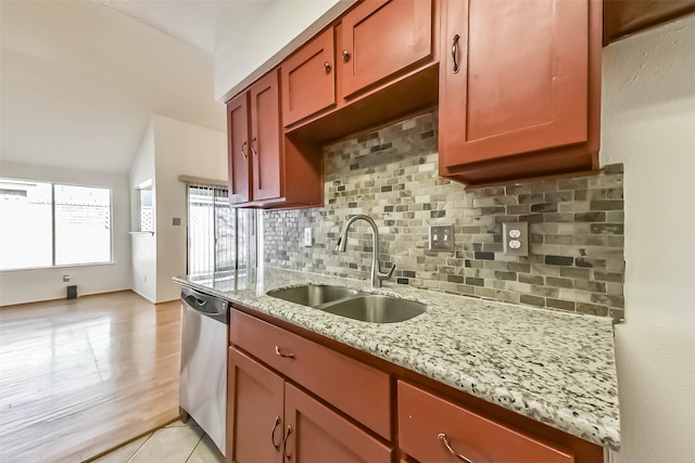 kitchen featuring backsplash, dishwasher, light stone counters, light tile patterned floors, and a sink