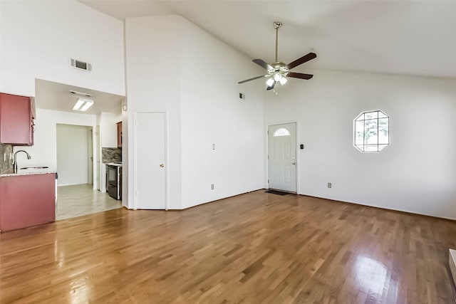 unfurnished living room with visible vents, light wood-style flooring, high vaulted ceiling, a ceiling fan, and a sink