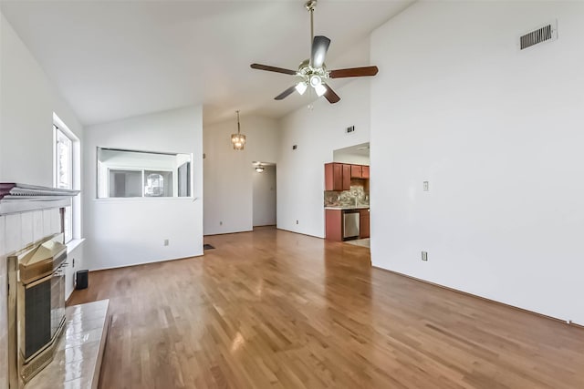 unfurnished living room with a ceiling fan, visible vents, light wood finished floors, high vaulted ceiling, and a glass covered fireplace