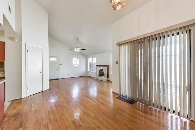 unfurnished living room with light wood finished floors, visible vents, a glass covered fireplace, high vaulted ceiling, and a ceiling fan