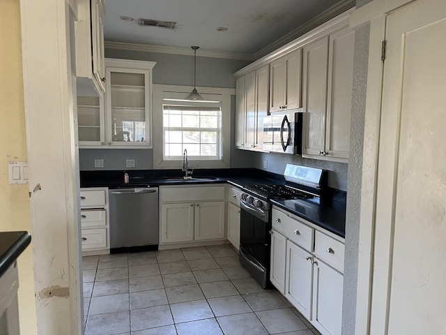 kitchen with dark countertops, appliances with stainless steel finishes, ornamental molding, white cabinetry, and a sink