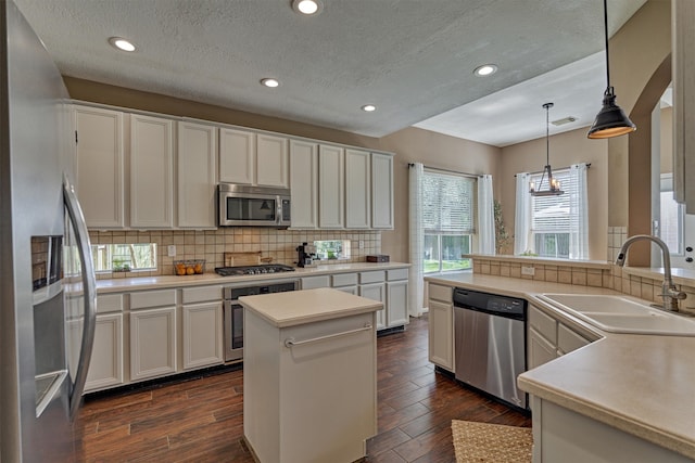 kitchen featuring dark wood finished floors, a sink, hanging light fixtures, appliances with stainless steel finishes, and tasteful backsplash