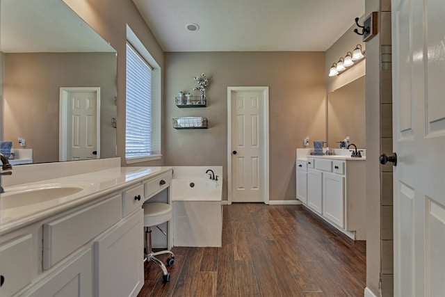 full bathroom featuring baseboards, two vanities, wood finished floors, a bath, and a sink