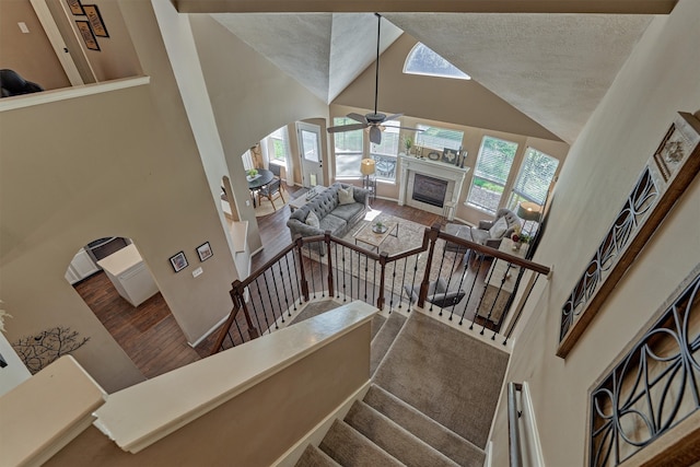 stairway with plenty of natural light, a fireplace, high vaulted ceiling, and wood finished floors