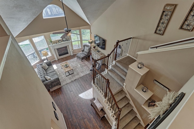 living room with stairs, wood finished floors, a glass covered fireplace, high vaulted ceiling, and a ceiling fan