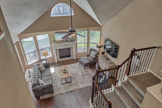 living area with a ceiling fan, a textured ceiling, wood finished floors, stairway, and a tile fireplace