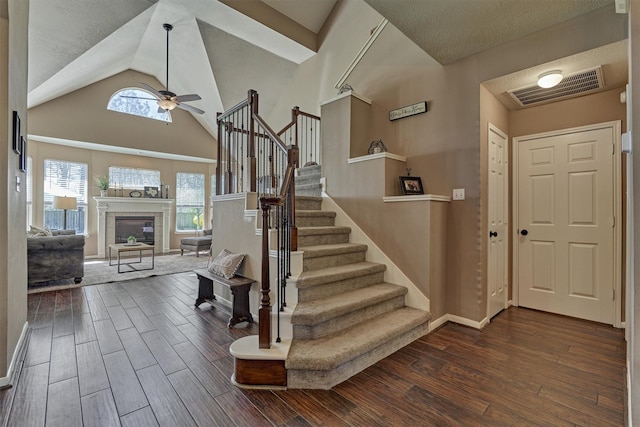 entryway with visible vents, dark wood-type flooring, stairway, ceiling fan, and a tile fireplace