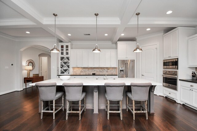 kitchen with arched walkways, beam ceiling, dark wood-style flooring, stainless steel appliances, and a sink