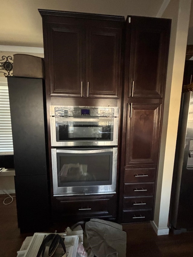 interior space featuring stainless steel double oven, dark brown cabinetry, and baseboards