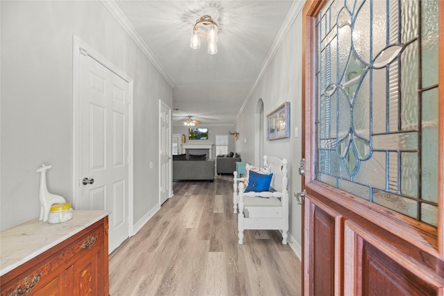 entryway with arched walkways, crown molding, a fireplace, light wood-style floors, and a ceiling fan