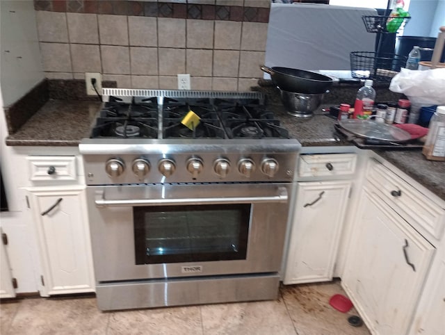 kitchen with tasteful backsplash, dark countertops, stainless steel stove, and white cabinetry