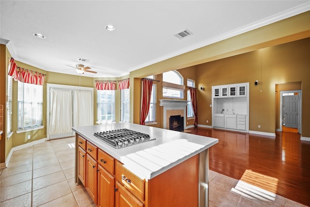 9406 Laurel Wind Ct, Houston, TX 77040 - kitchen with stainless steel gas cooktop, a lit fireplace, a ceiling fan, a center island, and light tile patterned flooring