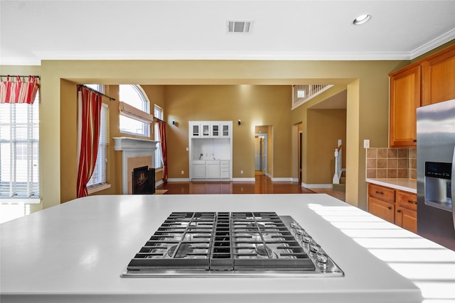 9406 Laurel Wind Ct, Houston, TX 77040 - kitchen featuring stainless steel appliances, a tile fireplace, light countertops, ornamental molding, and brown cabinets