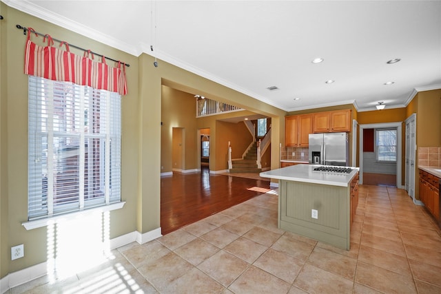 kitchen with backsplash, light countertops, ornamental molding, light tile patterned floors, and stainless steel fridge