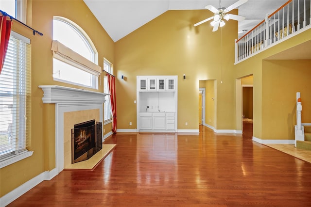 unfurnished living room featuring ceiling fan, baseboards, a tile fireplace, wood finished floors, and high vaulted ceiling