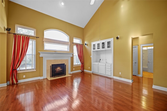 unfurnished living room with wood-type flooring, a fireplace, a wealth of natural light, and high vaulted ceiling