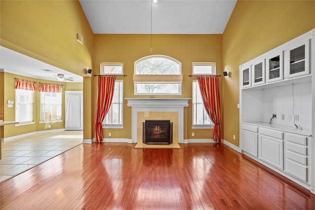 unfurnished living room with a wealth of natural light, visible vents, hardwood / wood-style flooring, ceiling fan, and a tile fireplace