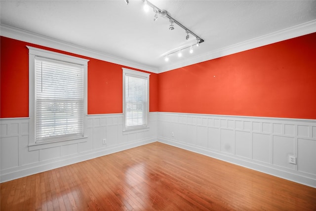 spare room featuring hardwood / wood-style floors, track lighting, ornamental molding, and wainscoting