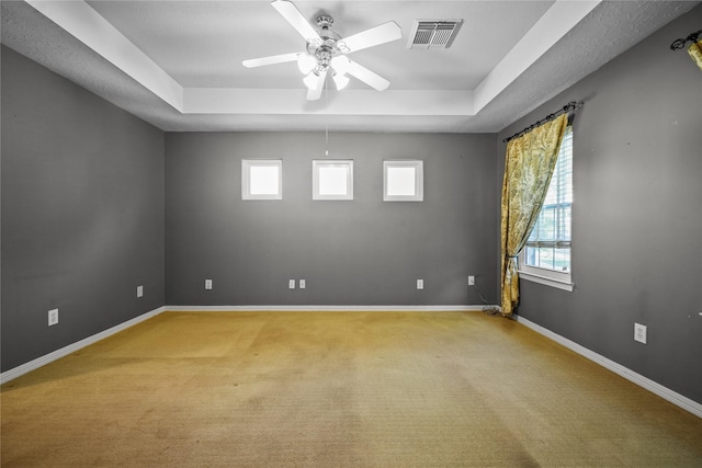 empty room featuring a tray ceiling, visible vents, baseboards, and light carpet