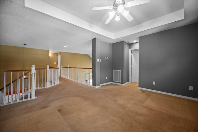 empty room with visible vents, baseboards, carpet floors, a raised ceiling, and a ceiling fan