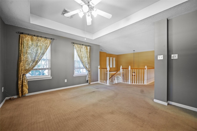 empty room with visible vents, a ceiling fan, a tray ceiling, carpet flooring, and baseboards