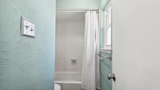 bathroom featuring a textured wall, shower / bath combo, and toilet