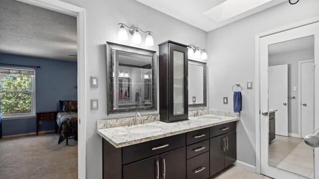 full bathroom featuring double vanity, a skylight, a sink, and ensuite bathroom