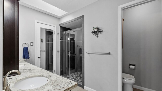 full bath featuring double vanity, a stall shower, baseboards, toilet, and a sink