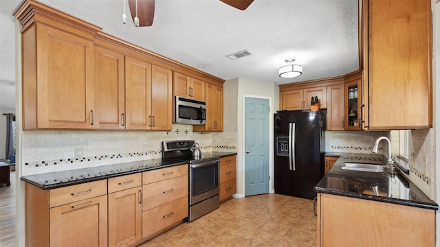 kitchen with visible vents, dark stone counters, glass insert cabinets, appliances with stainless steel finishes, and a sink