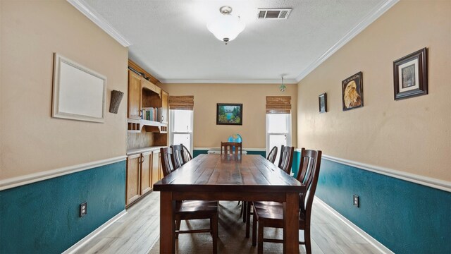 dining area with light wood-type flooring, visible vents, ornamental molding, and a textured wall