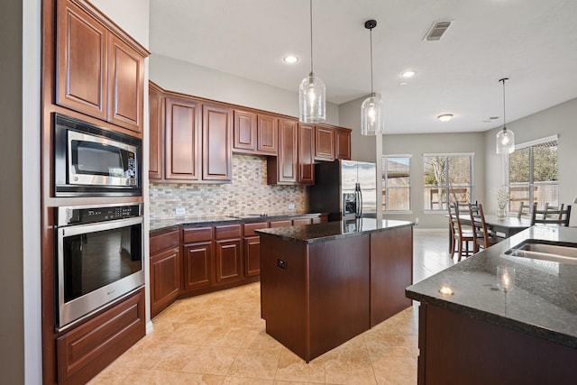 kitchen with decorative light fixtures, stainless steel appliances, tasteful backsplash, a kitchen island, and a sink