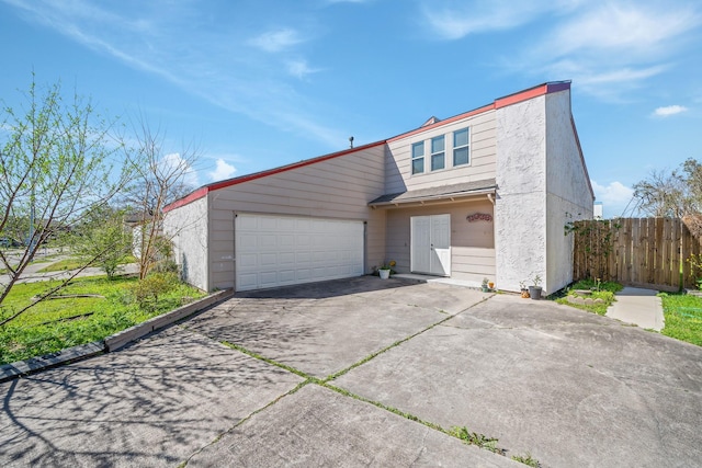 view of front facade featuring concrete driveway, an attached garage, and fence