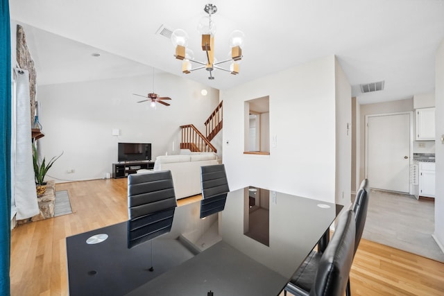 dining space with ceiling fan with notable chandelier, visible vents, light wood-style flooring, and stairs