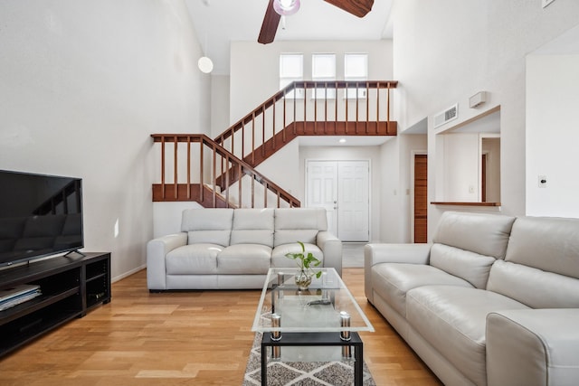 living area featuring visible vents, a ceiling fan, a towering ceiling, light wood-style flooring, and stairway