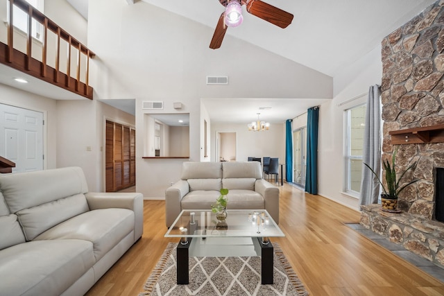 living room with high vaulted ceiling, a stone fireplace, light wood-type flooring, and visible vents