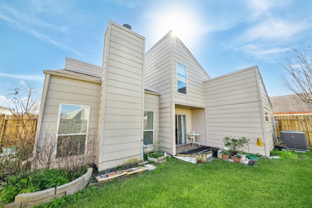 back of property with a chimney, fence, central AC, and a yard