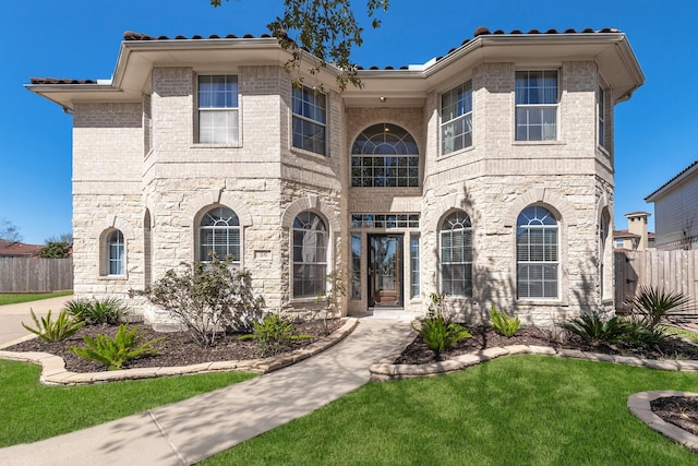 mediterranean / spanish house featuring a front yard, fence, and brick siding