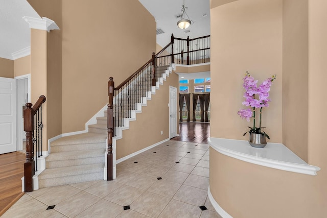 tiled foyer entrance featuring visible vents, a towering ceiling, baseboards, stairway, and decorative columns