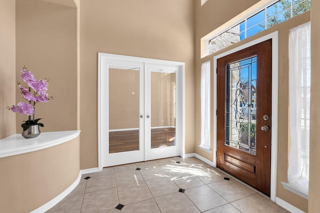 foyer entrance featuring a towering ceiling, tile patterned floors, baseboards, and french doors