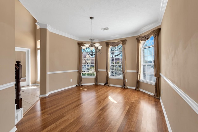 unfurnished dining area with a notable chandelier, visible vents, ornamental molding, wood finished floors, and baseboards