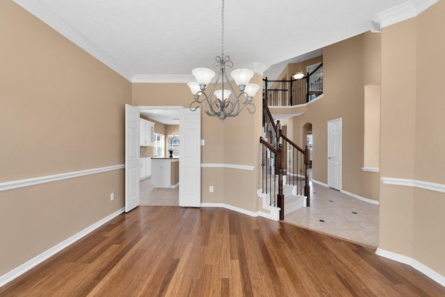 unfurnished dining area featuring baseboards, wood finished floors, an inviting chandelier, stairs, and crown molding
