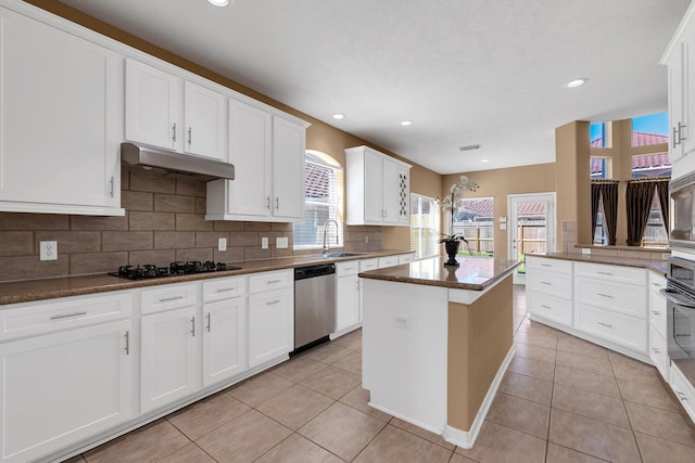 kitchen featuring stainless steel appliances, decorative backsplash, light tile patterned flooring, a sink, and under cabinet range hood