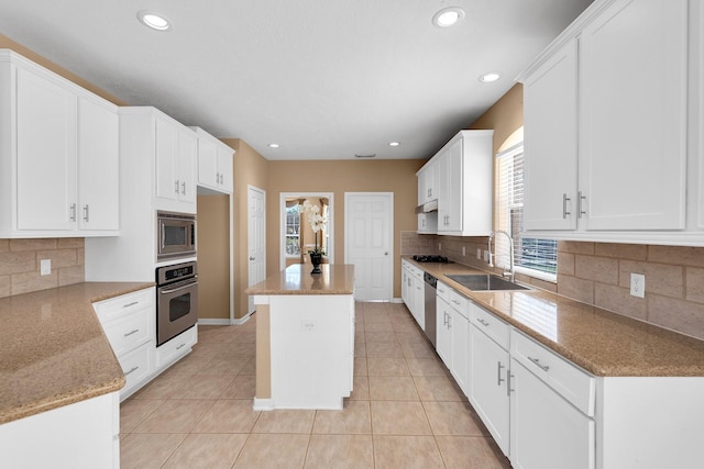 kitchen with light tile patterned floors, appliances with stainless steel finishes, light stone counters, a center island, and a sink